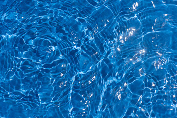 Blue water with ripples on the surface. Defocus blurred transparent blue colored clear calm water surface texture with splashes and bubbles. Water waves with shining pattern texture background.