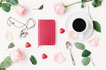 Romantic background with a cup of coffee, peach roses, red notebook, owl shaped clock, heart shaped candies on white background. Vintage tones, flat lay, top view