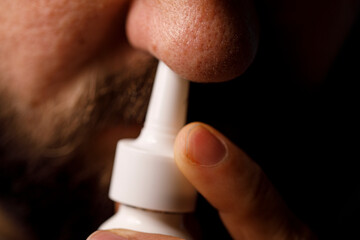 Close-up of a man using a nasal spray.  This image can be used to describe cold, flu, allergies or sinus issue