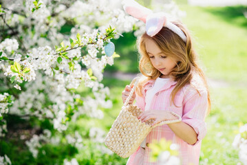 Easter egg hunt. Girl child Wearing Bunny Ears Running To Pick Up Egg In Garden. Easter tradition. Baby with basket full of colorful eggs.