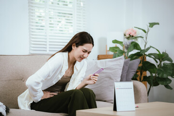 Fototapeta premium An Asian woman holding a blister pack of pills at home highlights healthcare, medication awareness, contraception, and daily health management in the context of modern lifestyles.
