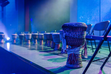Colorful traditional drums arranged on stage, illuminated by vibrant lights, creating an energetic...