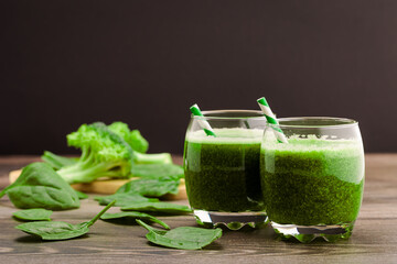 Fresh green juice made from spinach and broccoli served in glasses with straws on a wooden surface in the kitchen
