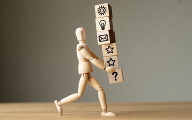 A wooden figure carrying a stack of blocks with various symbols on a wooden surface against a gray background