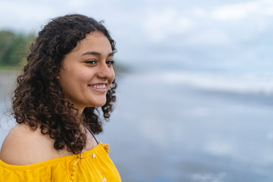 Close up portrait of a smiling young woman with curly hair and braces at the beach