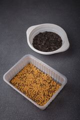 Mustard and sunflower microgreen seeds in plastic container with linen substrate on grey background. Closeup shot