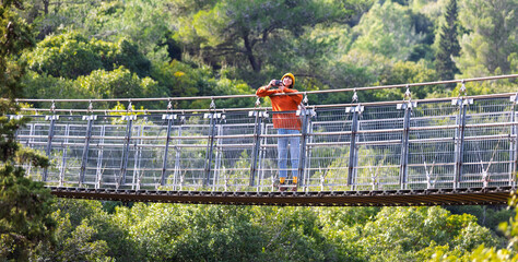 Travel and photography. A young woman with a camera and a backpack enjoys the view from the suspension bridge. Happy female tourist enjoying her trip.