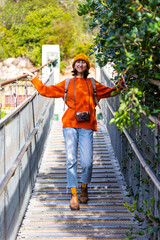 Travel and photography. A young woman with a camera and a backpack walks along a suspension bridge. Happy female tourist traveler enjoying her trip.