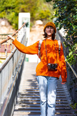 Travel and photography. A young woman with a camera and a backpack walks along a suspension bridge. Happy female tourist traveler enjoying her trip.