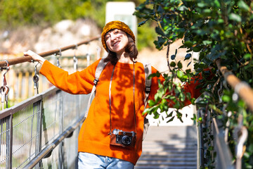 Travel and photography. A young woman with a camera and a backpack walks along a suspension bridge. Happy female tourist traveler enjoying her trip.