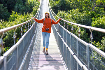 Travel and photography. A young woman with a camera and a backpack walks along a suspension bridge. Happy female tourist traveler enjoying her trip.