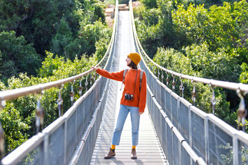 young woman with a camera and a backpack enjoys a walk along the suspension bridge. Happy female tourist enjoying her trip.