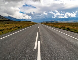 Fototapeta premium Asphalt road stretching towards mountains under dramatic cloudy sky