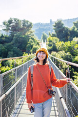 young woman with a camera and a backpack enjoys a walk along the suspension bridge. Happy female tourist enjoying her trip.