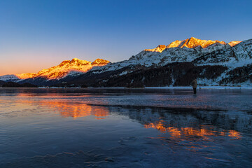 Naklejka premium Silser Lake (Silsersee) in winter with the frozen, snowless lake surface, which is called Black Ice, at the sunset.