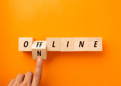 Hand flipping a wooden block to change the word ONLINE to OFFLINE on orange background. Top view of digital detox, mental health, work-life balance, and disconnect to reconnect business concept.