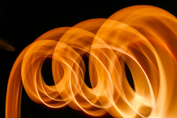 Abstract image featuring flowing light trails, creating curved lines with a warm, glowing tone. The light paints an organic, dynamic texture against a dark background