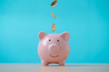 Golden coins drop to pink piggy saving on blue background for money saving to deposit into the...