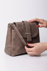 Elegant brown textured leather messenger bag with flap closure. Woman's hands with red nails adjusting a stylish crossbody purse isolated on white background. Professional fashion product photography.