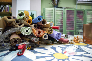 Creative workshop table covered with colorful rolls of wrapping paper and craft supplies. Post-holiday cleanup scene with leftover decorative materials, festive textures, and artistic workspace atmosp