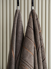 Two plush towels hanging on hooks against a textured wall, showcasing soft fabric and warm tones,...