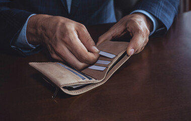 Male individual in a formal suit is organizing cards in a stylish wallet on a wooden table, showcasing attention to detail and personal finance management
