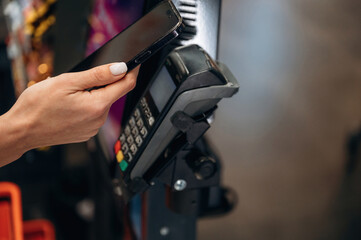 Hand holding smartphone above contactless payment terminal, showcasing modern technology in retail environment with vibrant colors and dynamic atmosphere