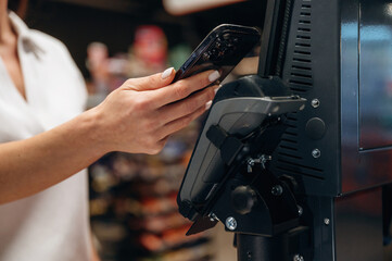 Woman using smartphone to make contactless payment at a modern checkout kiosk, showcasing convenience and technology in retail environment