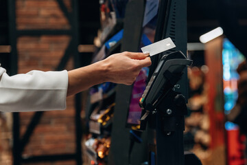 Hand of a customer using a credit card at a payment terminal in a retail store, showcasing modern...