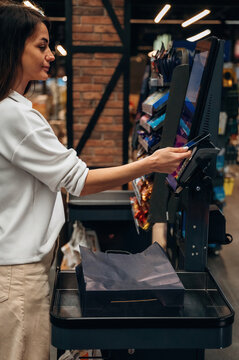Young woman using self-checkout kiosk in a modern grocery store, showcasing technology and convenience in retail shopping experience
