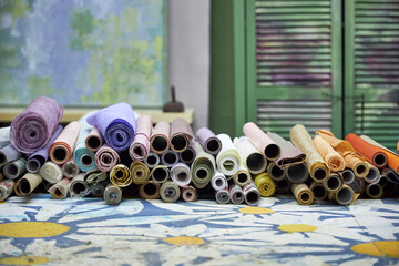Stacks of colorful wrapping and craft paper rolls arranged on a creative workshop table. Artistic workspace with decorative materials, textures, and post-holiday gift wrapping supplies ready for reuse