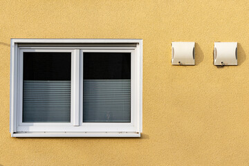 Window and air vents on yellow wall in urban setting