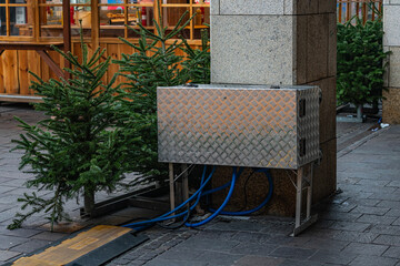 Metal box with pipes near Christmas trees in a city square
