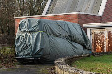 Large car covered with tarp near a building in a quiet area