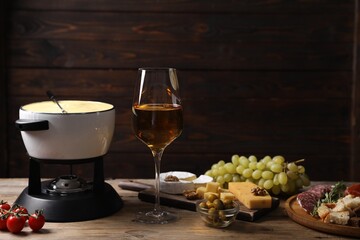 Fondue with tasty melted cheese, snacks and wine on wooden table. Space for text