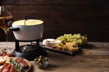 Fondue with tasty melted cheese, snacks and wine on wooden table. Space for text