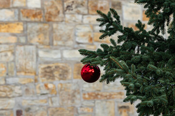 Decorative red ornament hangs from a green pine tree branch