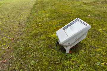 Light fixture sits on grass next to a path in a park on a cloudy day