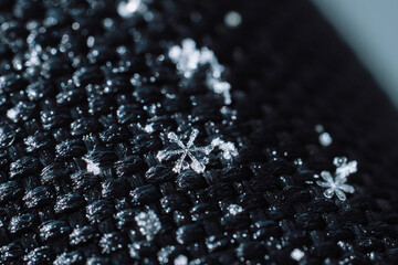 Macro snowflake crystal on black knitted fabric. High quality photo
