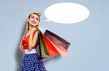 Black Friday Sales concept - beautiful cute blond woman in pinup pin-up dress holding carrying colourful shopping bags isolated grey gray background with empty mockup speech bubble. Mock up ad image