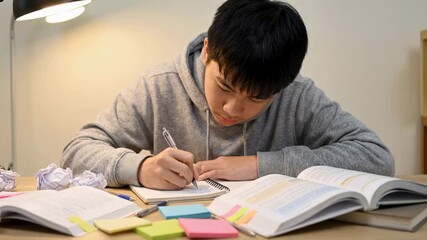 Teenage student studying at desk with textbooks and notes under lamp light, preparing for exams with focus and concentration in evening