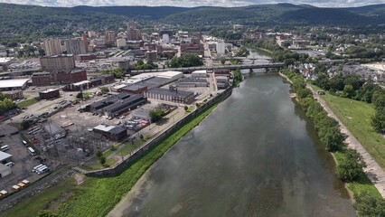 Binghamton city in New York State skyline with downtown buildings and business activity beside river in summer sunlight  
