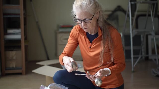 A mature woman inspects silver cutlery that belonged to her family, reflecting on memories and the importance of heirlooms and legacy.