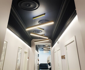 Modern hallway interior design with black ceiling and linear pendant lights arrangement creating zigzag pattern leading to waiting area with dark sofa and round mirror