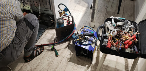 Person repairing refrigerator compressor with gas tanks, refrigeration tools, and copper pipes,...