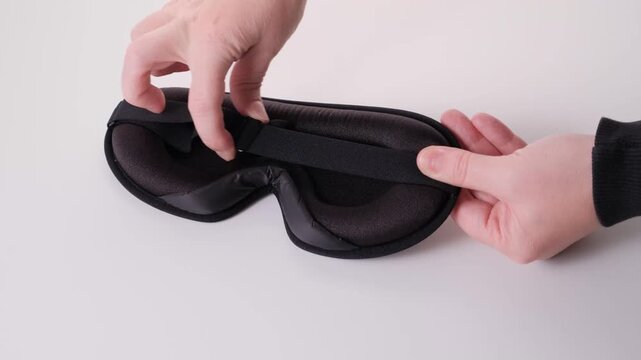 Hands adjusting a soft sleep mask with a strap, demonstrating the process of securing the mask for comfort and effective light blocking during rest or sleep