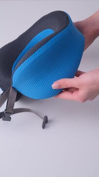Hand demonstrates the flexible design of a blue and black travel neck pillow, showcasing its adjustable features and ergonomic shape for comfort during travel