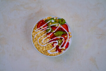 Delicious yogurt bowl topped with vibrant sliced strawberries, fresh kiwi pieces, and a generous drizzle of creamy white topping over textured oats.