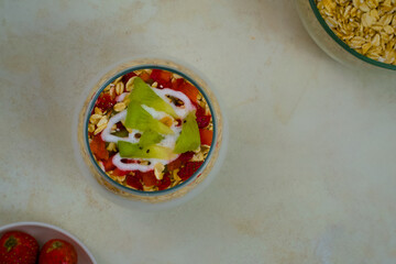 Overhead view of a vibrant glass bowl layered with healthy overnight oats, fresh strawberries, sliced kiwi fruit, and creamy yogurt topping