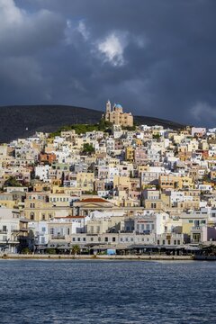View of the town of Ermoupoli with pastel-coloured houses and the sea, on the hill Anastasi Church or Church of the Resurrection, dramatic cloudy sky, Ermoupoli, Syros, Cyclades, Greece